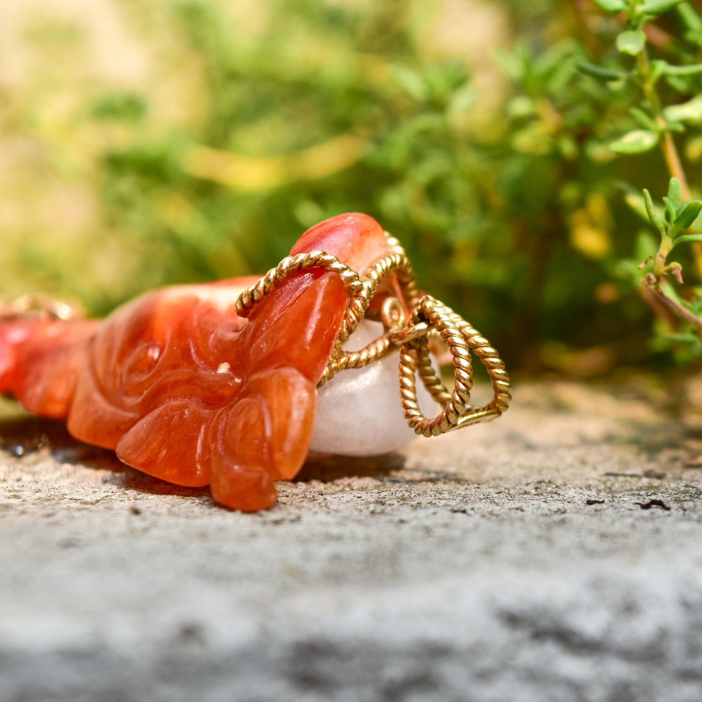 Carved red jade pendant featuring a Buddha figure wrapped in 14K yellow gold wire, set against a natural green background.