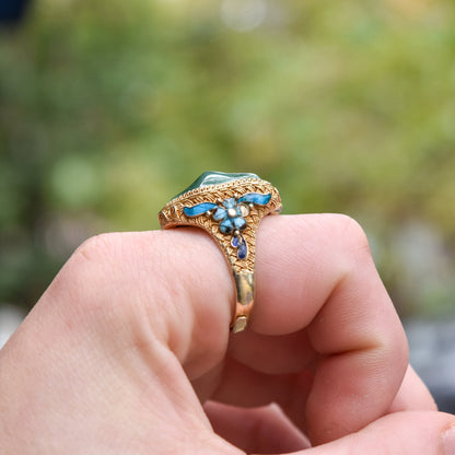 Intricate Chinese export vermeil silver adjustable ring with floral enamel designs and turquoise cabochon gemstone, held between fingers to show detail, with blurred natural background.