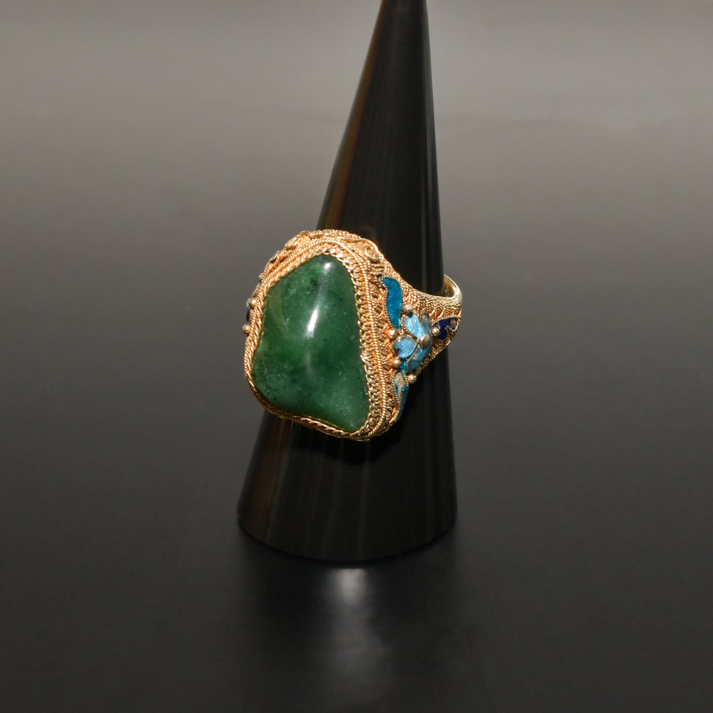 Antique Chinese export silver gilt ring featuring a natural jade stone cabochon accented with vibrant blue enamel and floral motifs in an adjustable design to fit ring sizes 7 to 11 US.