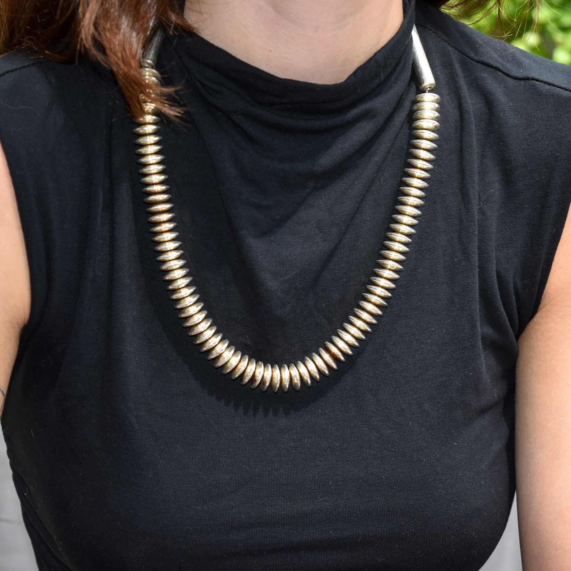 Modernist heavy sterling silver Navajo pearl necklace with saucer-shaped beads worn by a person in a black sleeveless top, showing the necklace resting across their chest and shoulders against the dark fabric background.