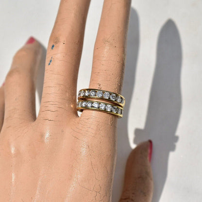 Close-up of hand wearing two gold channel set diamond rings, casting shadow on white surface