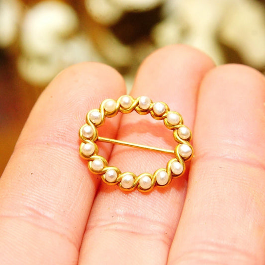 14K gold pearl wreath brooch pin held in hand, small oval shaped pin with gold ribbon setting and encrusted with pearls, 22mm in size, close up view of the pin against blurred background.