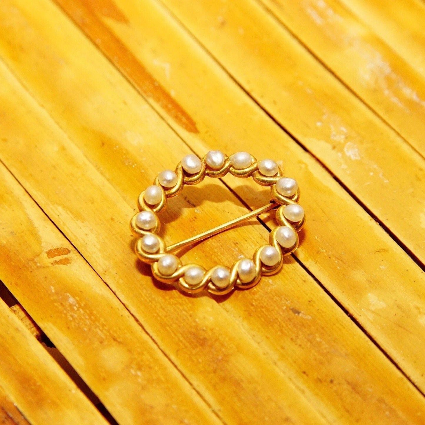 14K gold oval pearl wreath brooch pin with pearls set in a ribbon design, small scarf pin measures 22mm, shown on wooden background