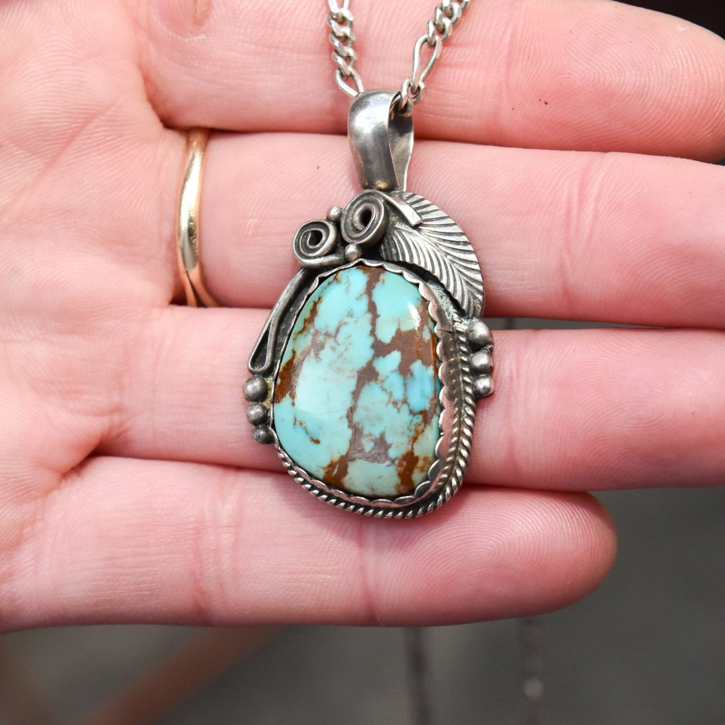 Signed Native American sterling silver pendant featuring a turquoise cabochon stone with leaf and swirl motif designs, measuring 1.75 inches long.