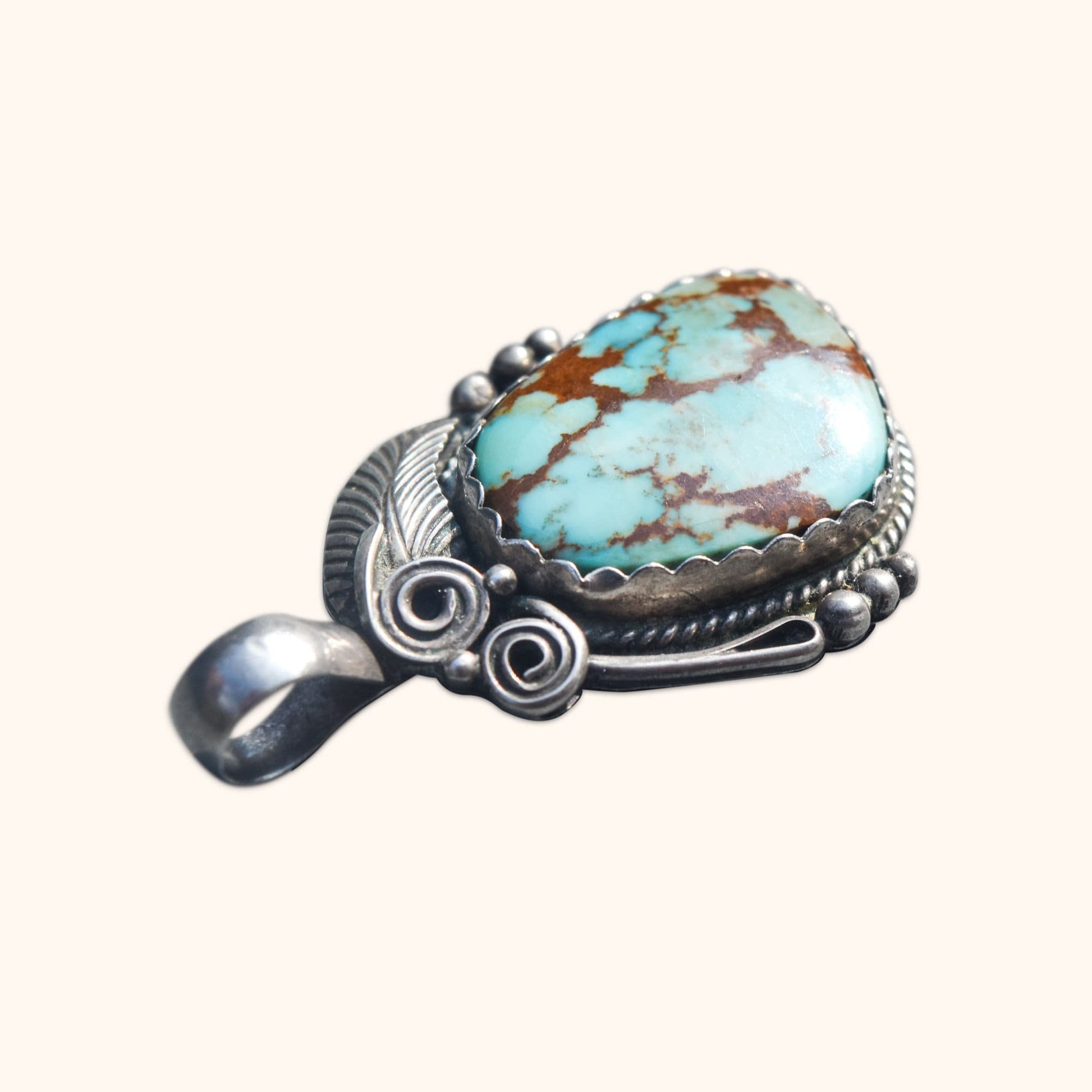 Navajo sterling silver pendant with swirl motifs featuring a blue turquoise stone, measuring 1.75 inches long.