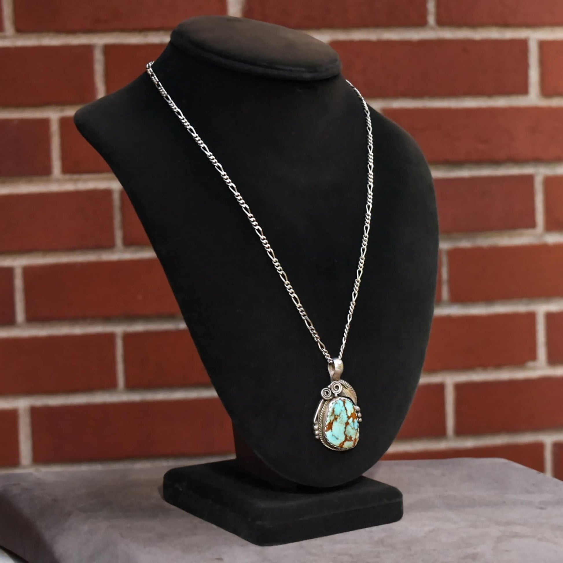 Signed Navajo sterling silver turquoise pendant necklace with leaf and swirl motifs on black velvet jewelry display stand