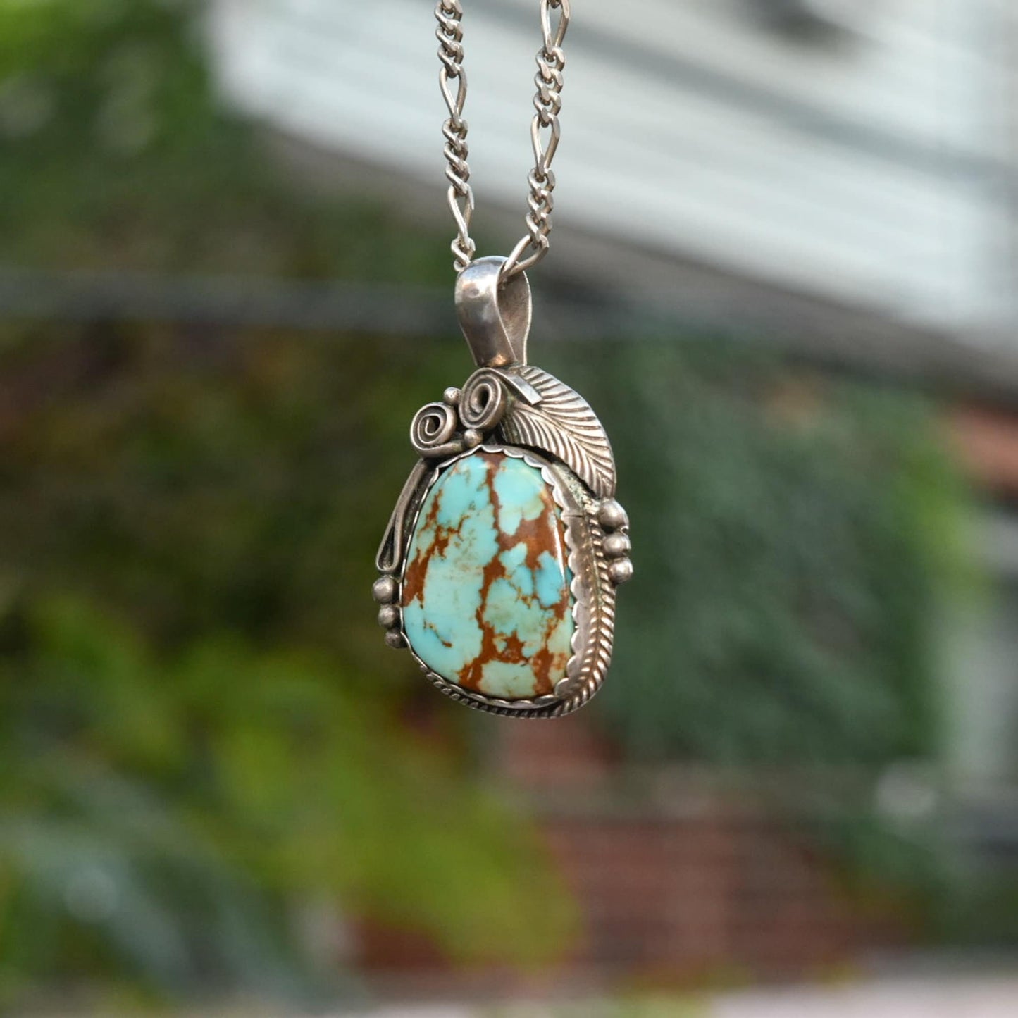 Native American sterling silver pendant necklace featuring natural turquoise stone with leaf and swirl motifs, signed Navajo jewelry measuring 1.75 inches long