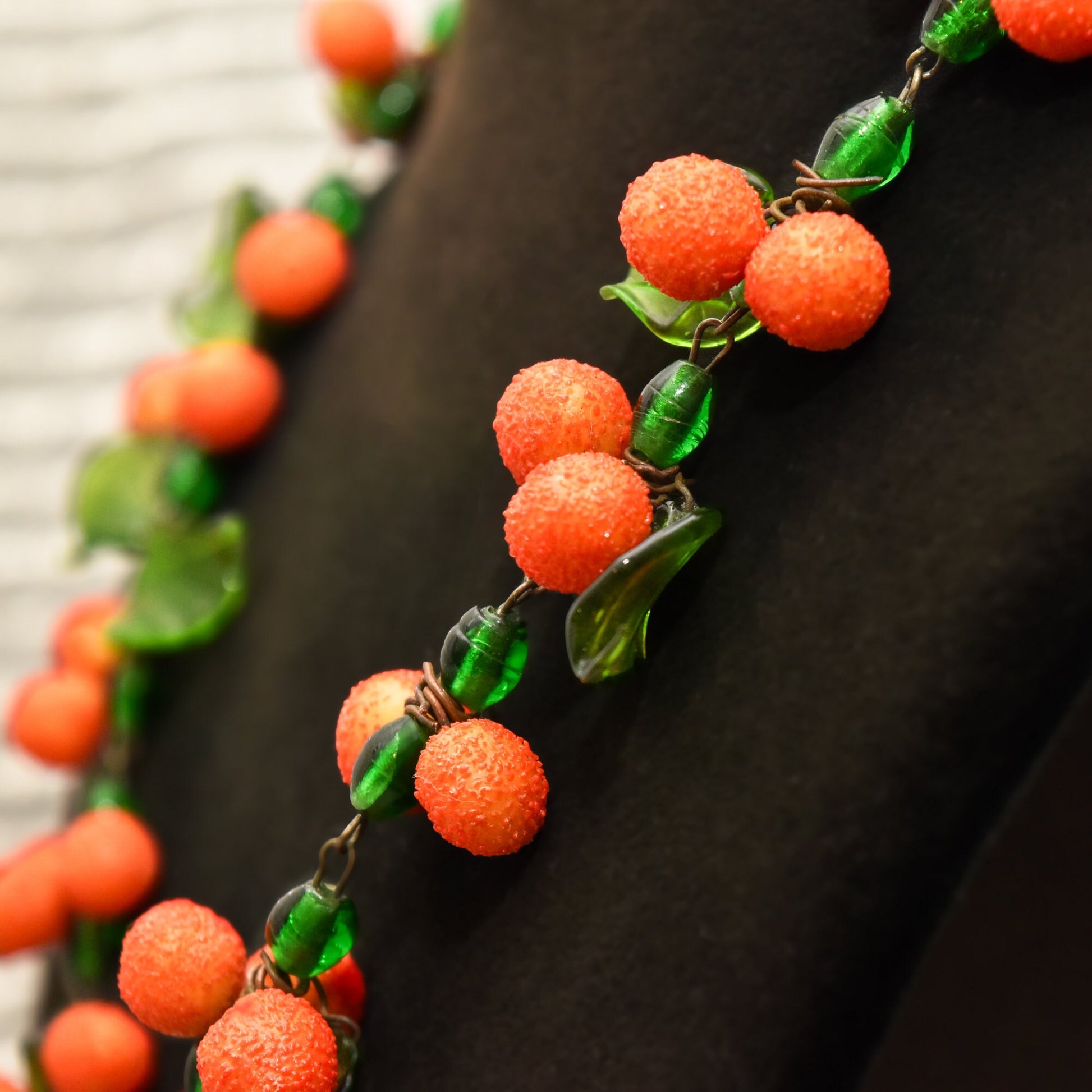 Red orange textured Murano glass berry beads on green leaf accented stems, forming a long festive Venetian glass necklace against a black background