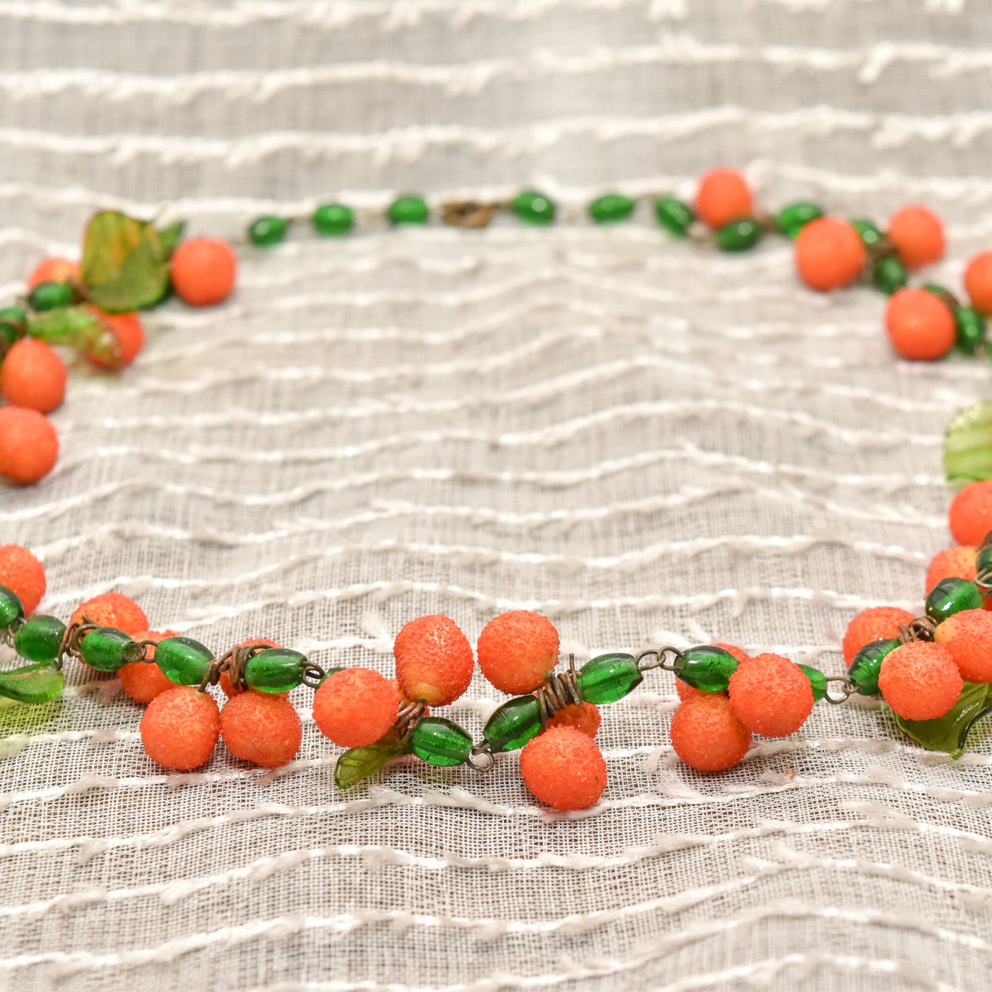 Vintage Venetian glass orange berry necklace on textured linen background, vibrant coral orange round glass beads and green glass leaves, festive Italian glass bead jewelry