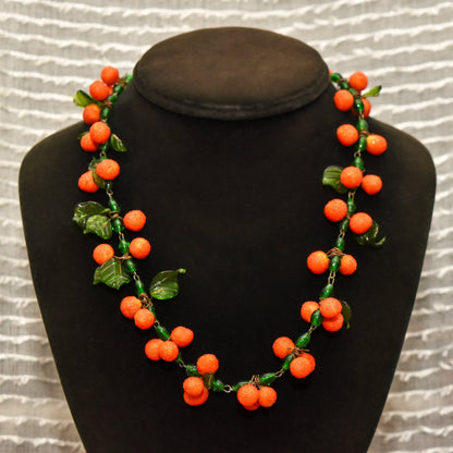 Venetian glass orange berry necklace with green leaves on black bust display against wavy white background