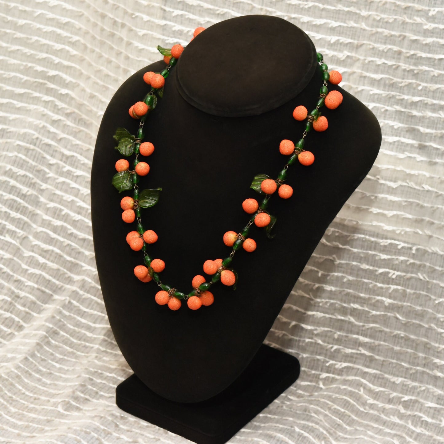 Vintage Italian orange glass berry bead necklace displayed on black velvet jewelry bust against textured white background