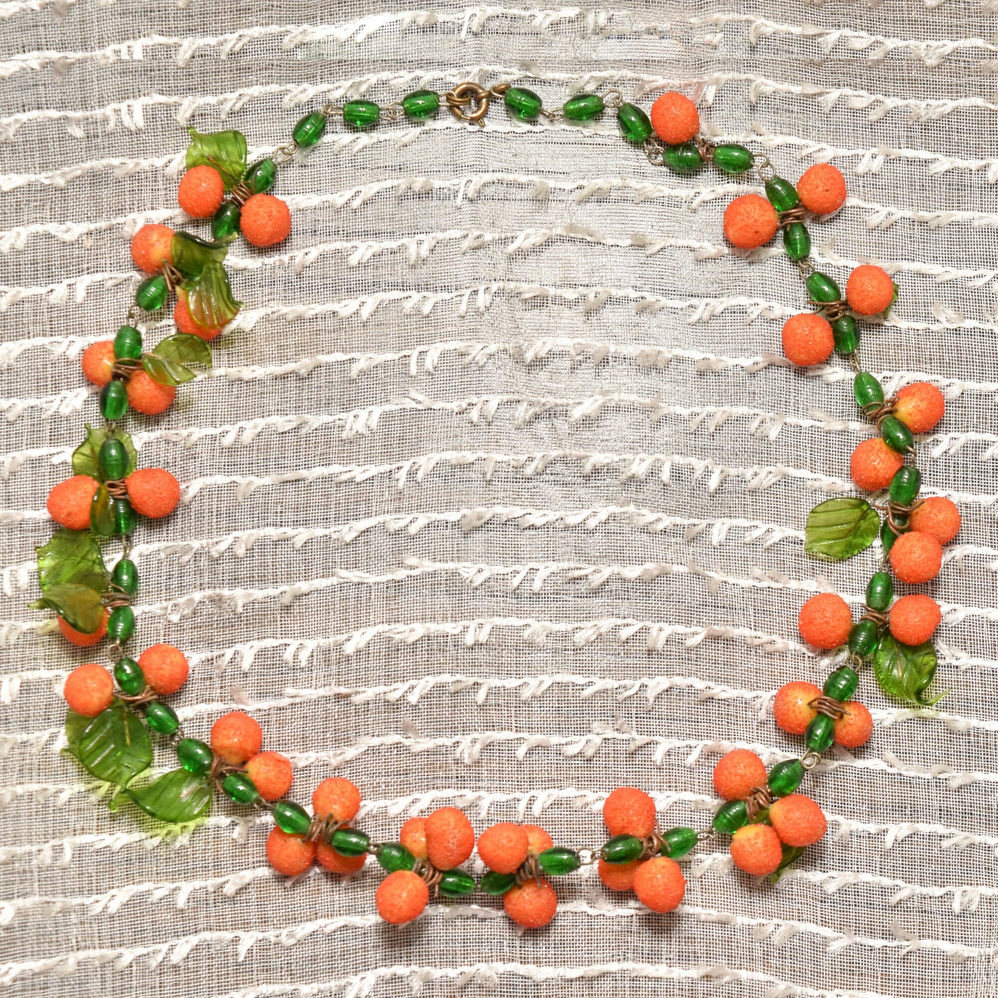 Orange venetian glass berry necklace arranged in circular wreath shape on textured beige fabric background