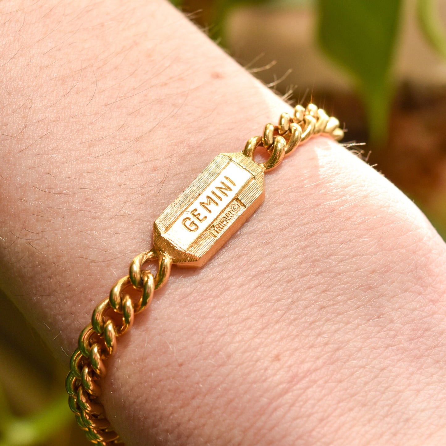 Gold-tone vintage Trifari bracelet with Gemini zodiac sign on hexagonal charm, featuring a 5mm curb link chain, astrology-themed jewelry, worn on wrist, with a length of 7 inches.
