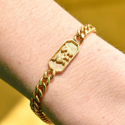 Gold tone vintage Trifari Gemini zodiac sign bracelet on wrist with 5mm curb link chain, astrology-themed jewelry, 7 inches long.