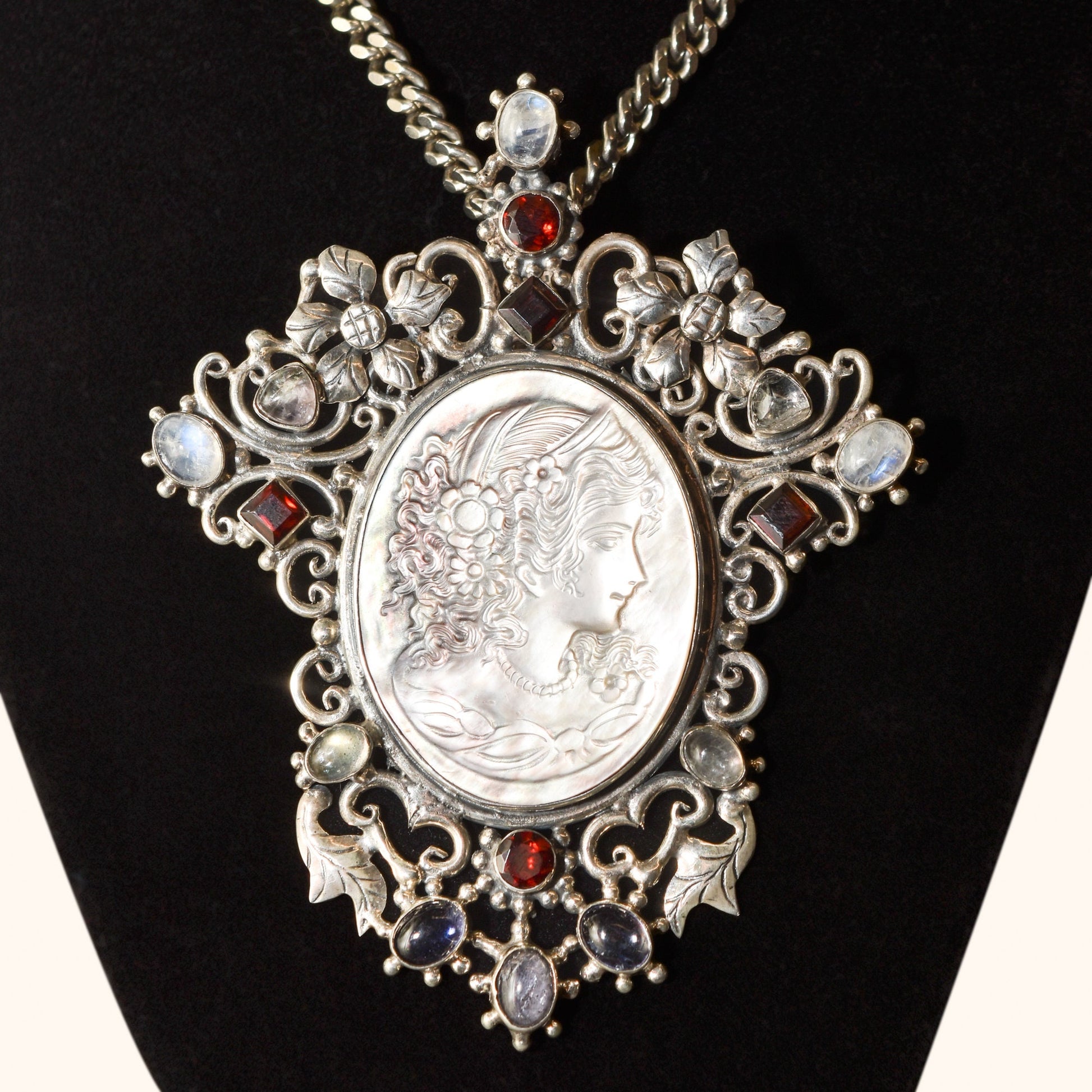 Victorian-style cameo pendant brooch in sterling silver with large ornate multi-stone design, measuring 4 inches long, displayed on a black background.