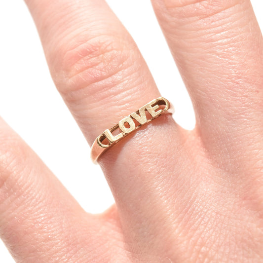 14K yellow gold 'LOVE' stacking ring on finger, minimalist Valentine's Day gift, size 6.75 US.