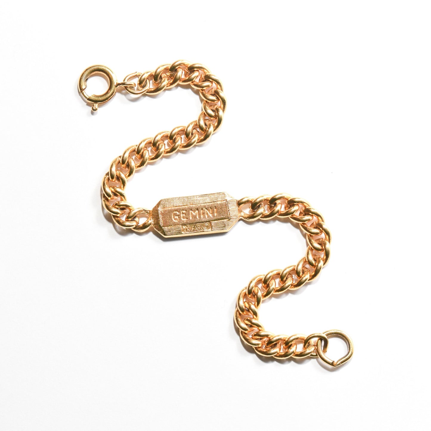 Vintage Trifari Gemini zodiac sign bracelet in gold tone with 5mm curb link chain on a white background, astrology-themed jewelry measuring 7 inches long.