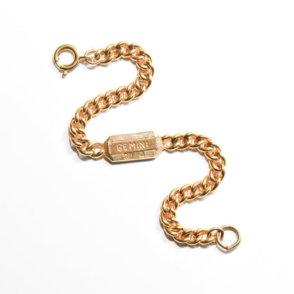 Vintage Trifari Gemini zodiac sign bracelet in gold tone with 5mm curb link chain on a white background, astrology-themed jewelry measuring 7 inches long.