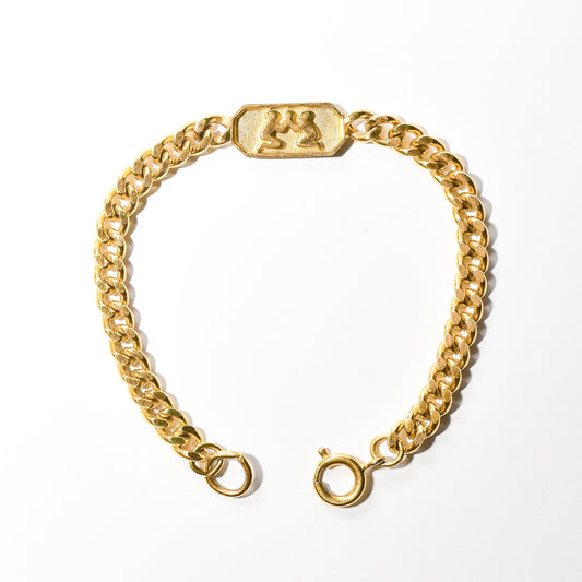 Vintage Trifari Gemini zodiac sign bracelet in gold tone with 5mm curb link chain on a white background, astrology-themed jewelry measuring 7 inches in length.