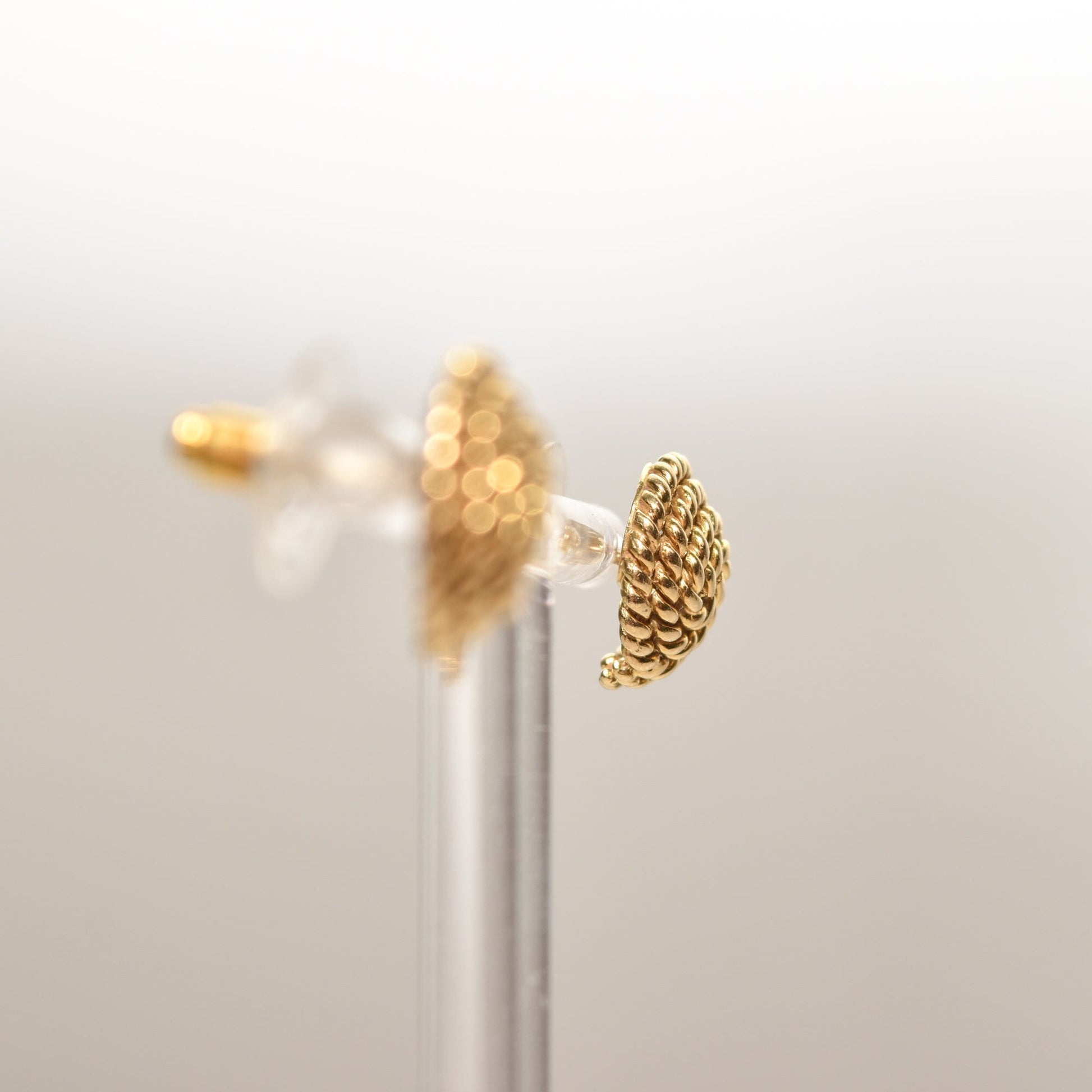 Alt text: Tiffany & Co Schlumberger 18K gold woven button stud earrings with coiled rope design displayed on a clear stand, showcasing estate jewelry measuring 14.5mm in a soft focus background.