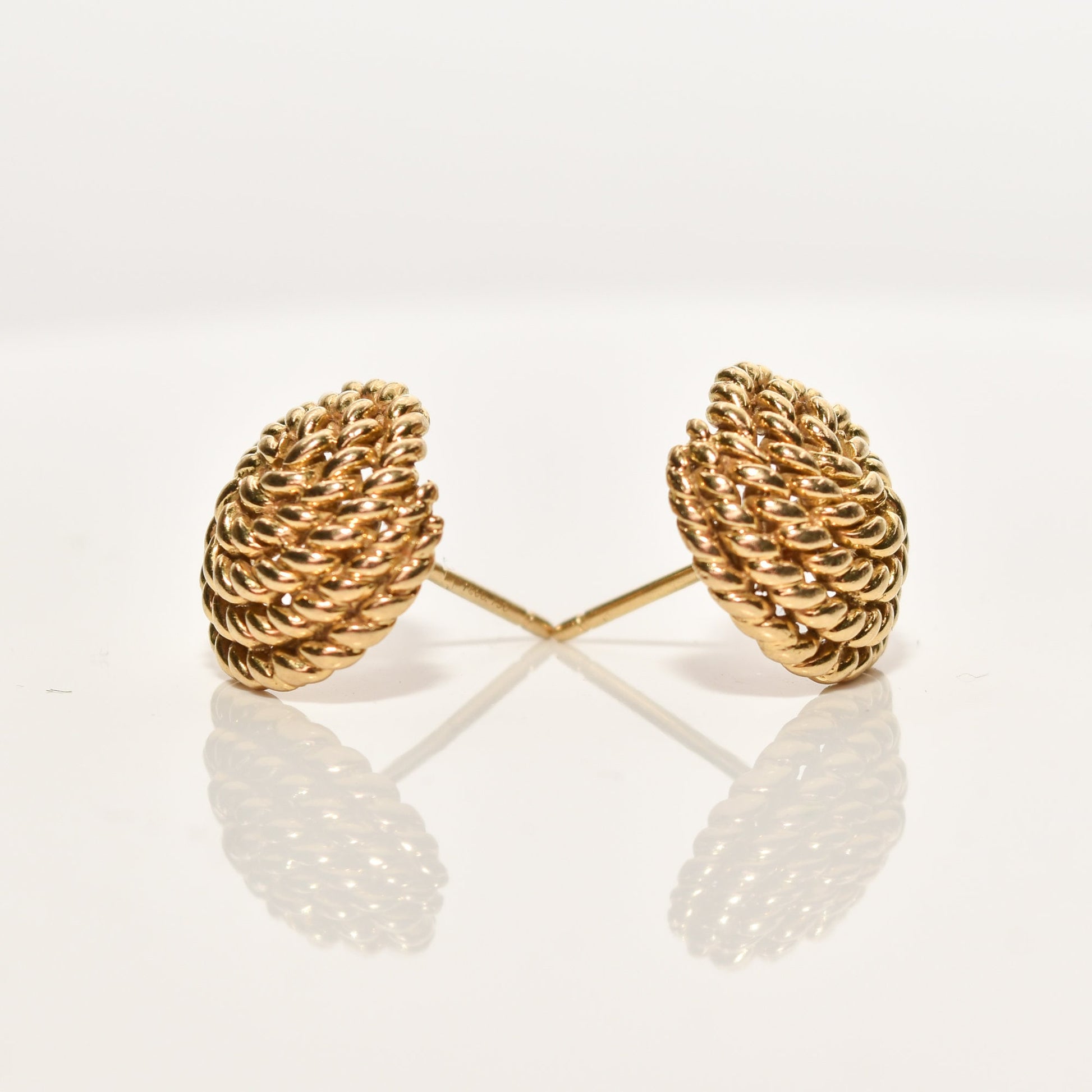 Alt text: "Tiffany & Co Schlumberger 18K gold woven button stud earrings with coiled rope design, positioned side by side with reflection on a shiny surface, measuring 14.5mm, from an estate jewelry collection.