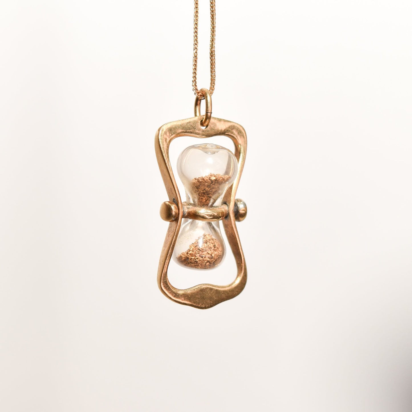 14K gold hourglass pendant with movable swivel mechanism and sparkling gold dust, estate jewelry piece measuring 36mm, suspended from a gold chain.