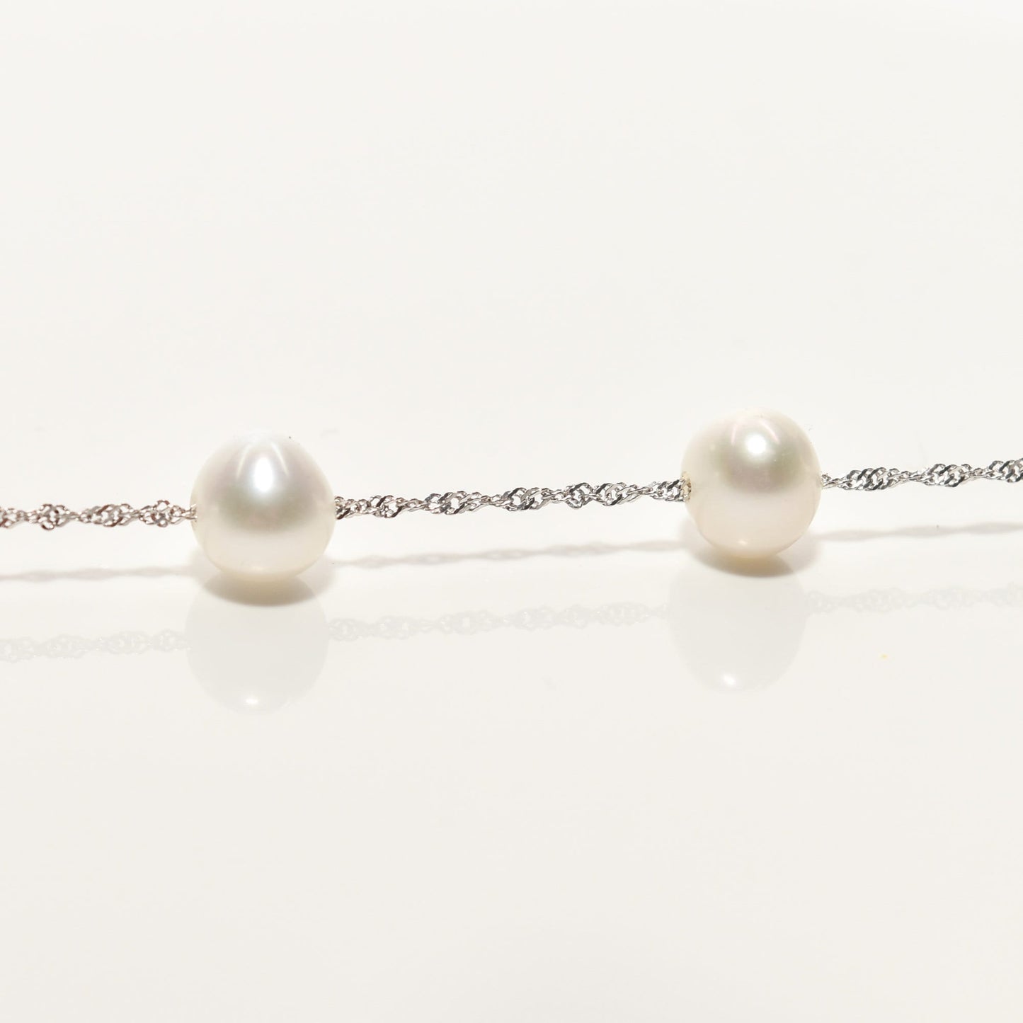 White pearl choker necklace in 14k white gold with pearl station design on a reflective surface, measuring 17.75 inches in length