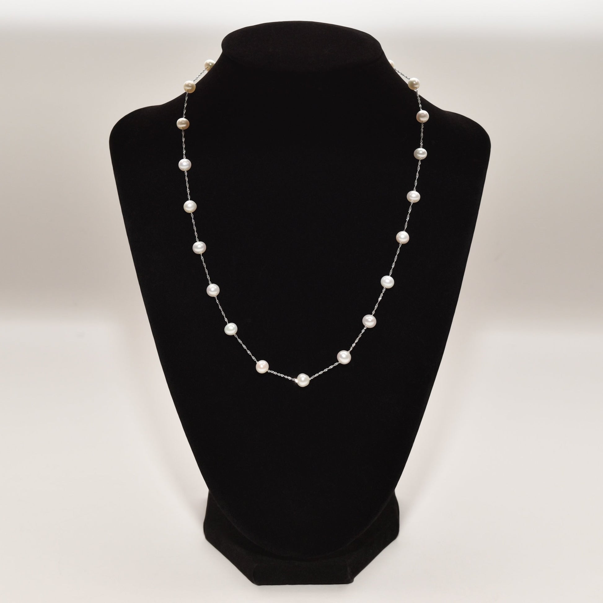 White pearl choker necklace in 14K white gold on a black display stand, featuring evenly spaced pearls in an elegant station design, measuring 17.75 inches in length.