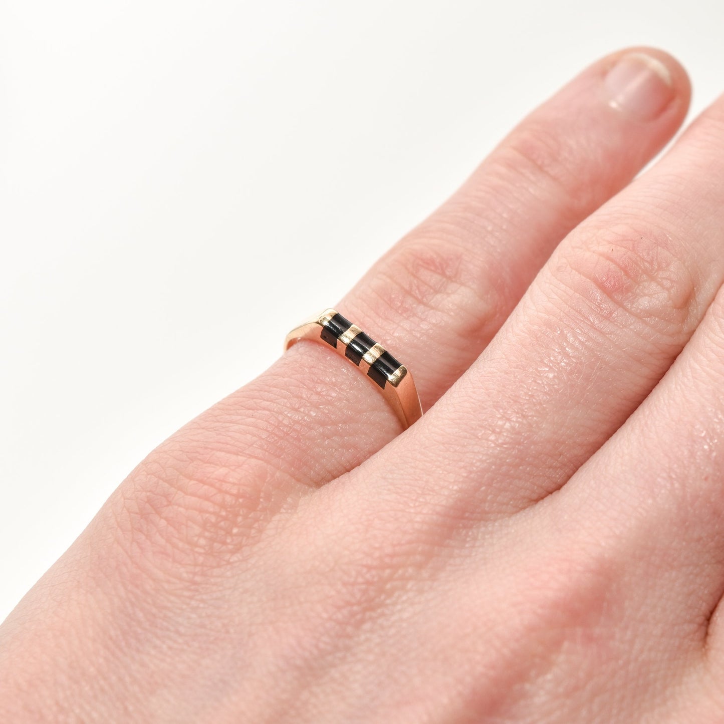 Close-up of a hand wearing a minimalist 14K black onyx inlay ring on a striped yellow gold band, size 5.5 US.
