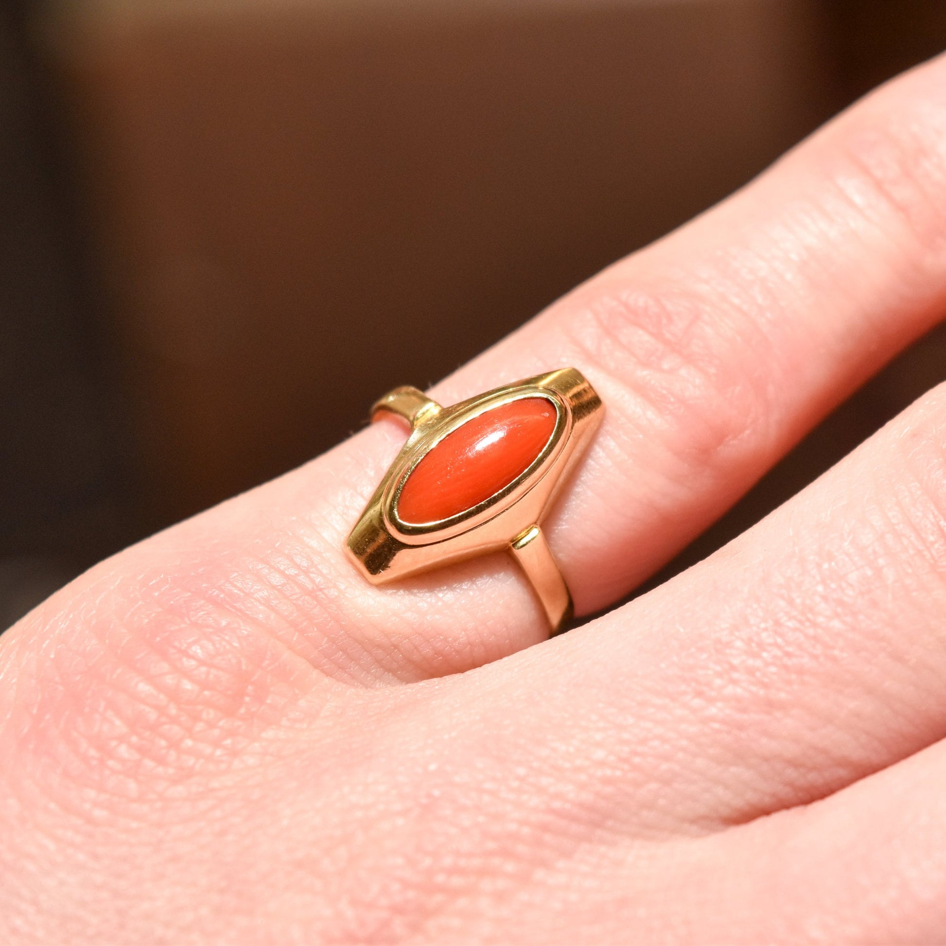 Close-up of a 18K yellow gold ring with marquise-cut red coral on a finger, size 5.25 US.
