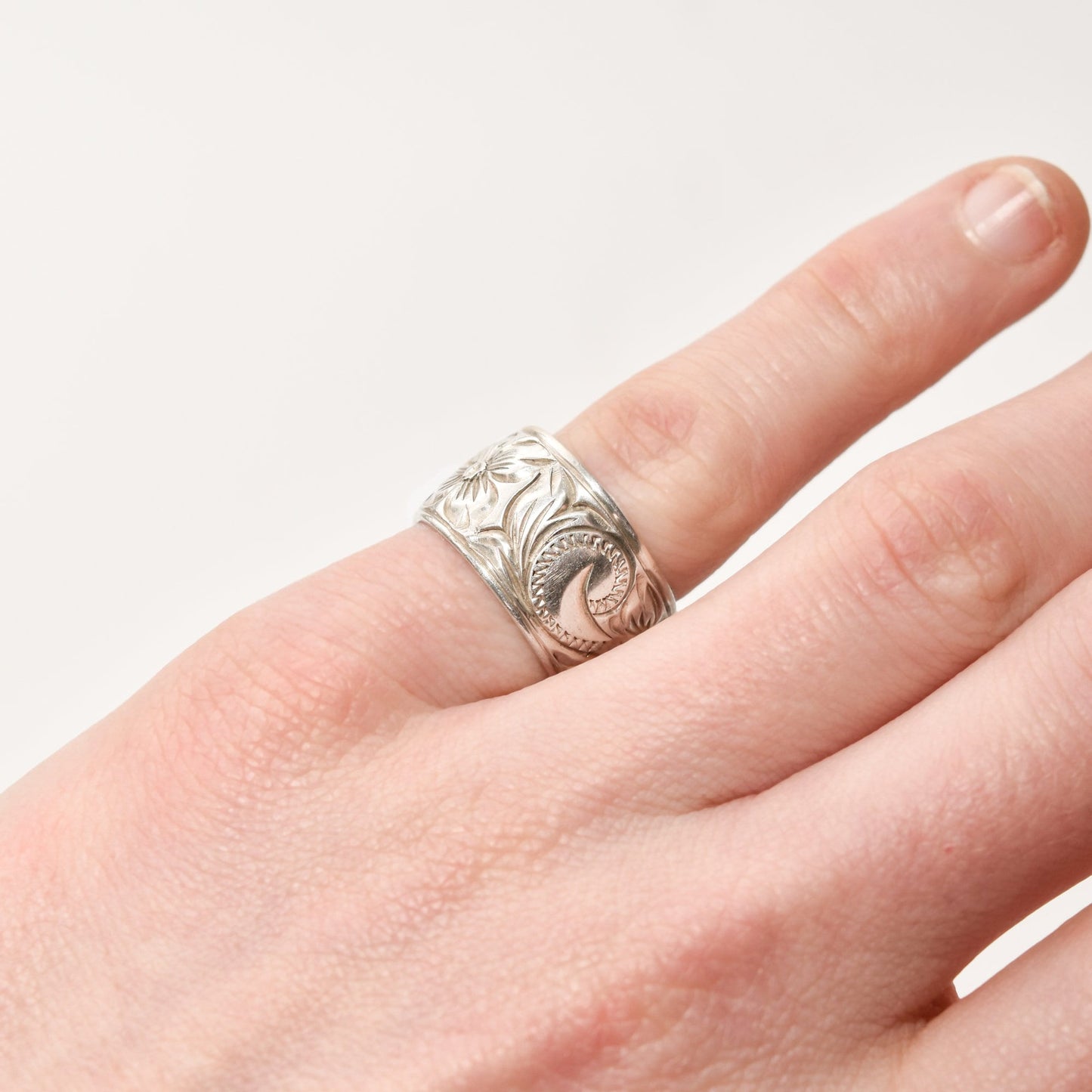Floral engraved sterling silver band ring 11.5mm wide in Art Nouveau style, size 6 US, displayed on a finger against a white background